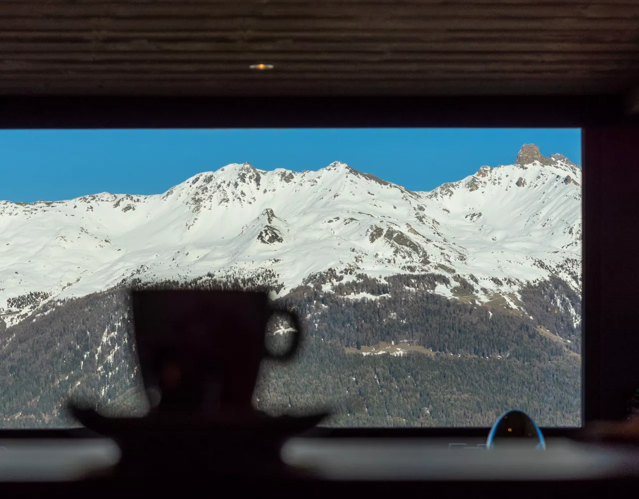 Tasse de café devant la baie vitrée et les montagnes enneigées